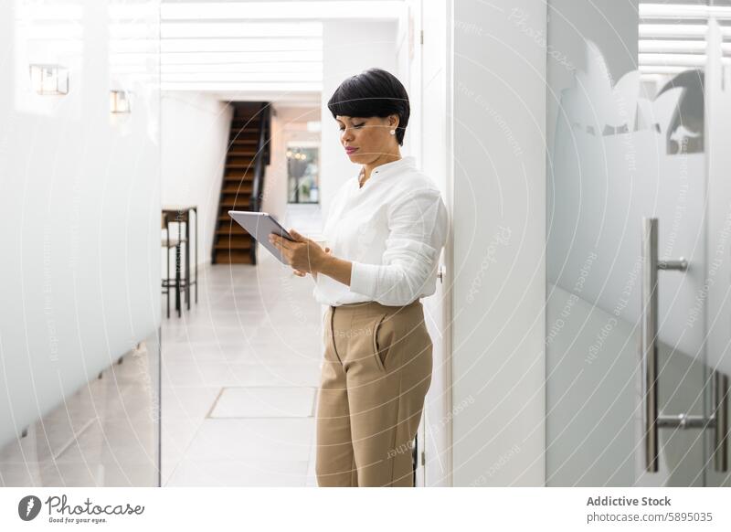 Professional woman using tablet in modern corridor professional office business technology productivity focus digital device work corporate attire white blouse