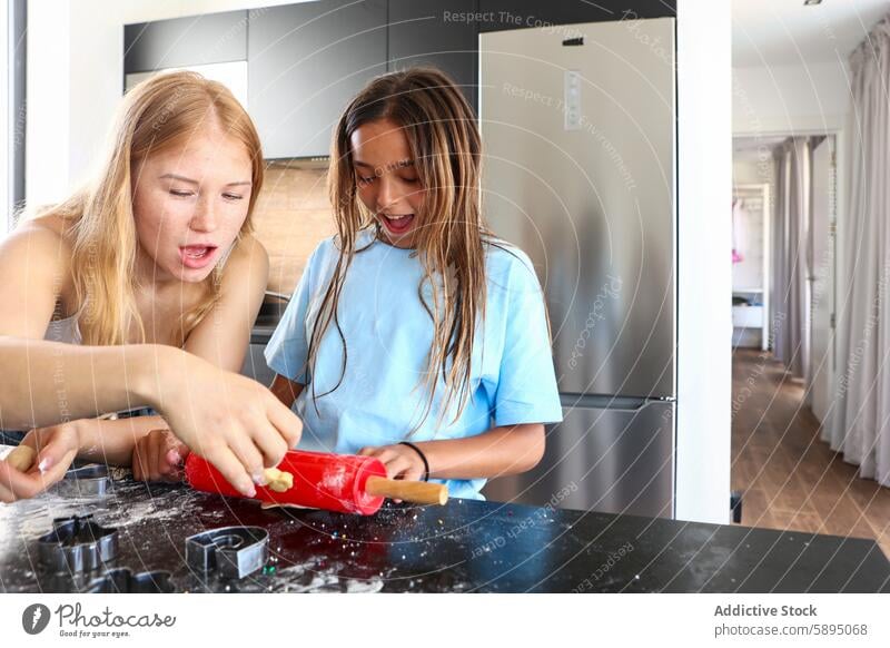 Two sisters baking cookies in a home kitchen triplet cooking rolling pin dough playful sibling family engagement activity enthusiasm joy learning flour mess