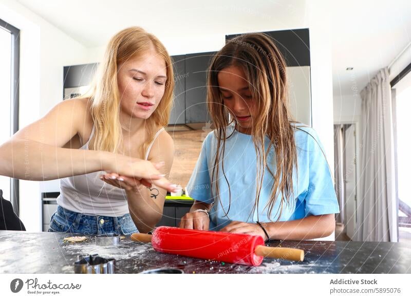 Sisters baking together in a modern kitchen teamwork cooking dough rolling pin ingredient measuring sprinkling togetherness casual indoor activity family