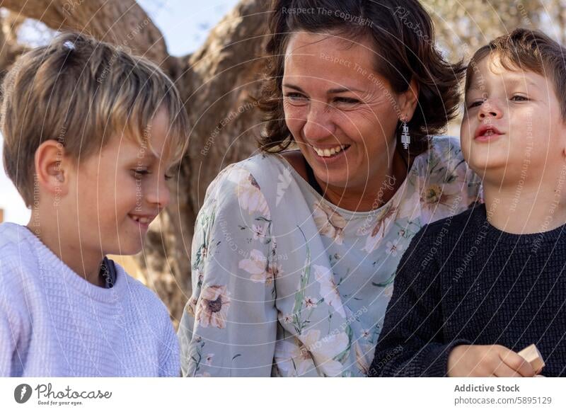 Mother and sons enjoying a playful moment outdoors in autumn family mother park smile engaging affectionate nature interaction maternal siblings brother leisure