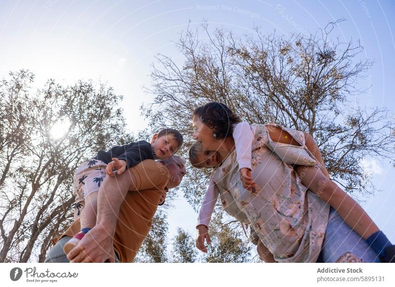 Family enjoying outdoor playtime at a park in autumn family father mother sons boys siblings nature piggyback tree enjoyment bonding looking at each other