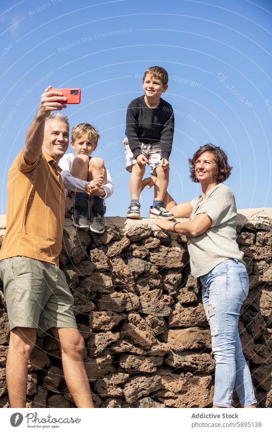 Happy family taking a selfie together outdoors sunshine happy father smile mother sons smartphone togetherness bonding leisure fun childhood parent siblings