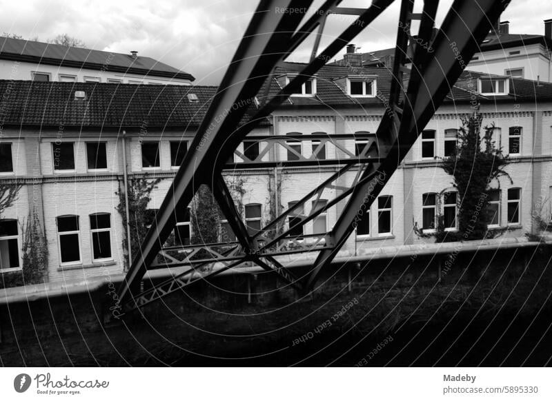 Steel girders of the Wuppertal suspension railroad and row of houses with restored old buildings in rainy weather in Wuppertal in the Bergisches Land in North Rhine-Westphalia in neo-realistic black and white