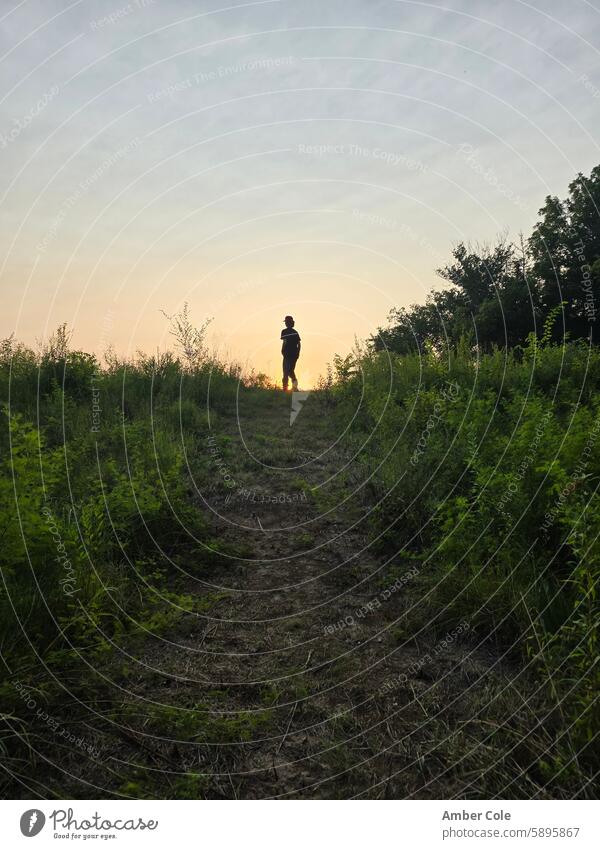 Male teen at the top of grassy hill at sunset sunset sky male teenager Sunset over hill scenic outdoors countryside Male at sunset