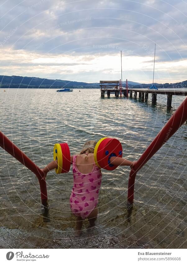 Little girl in pink swimsuit with water wings gets into the lake Lake Lake Attersee bathe Swimming & Bathing be afloat Water wings Footbridge Back-light