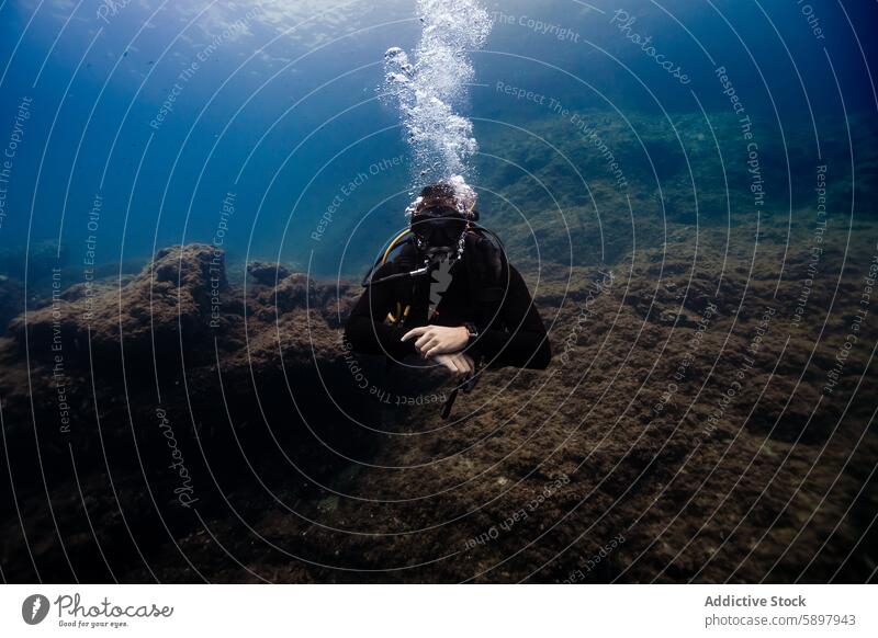 Scuba diver exploring underwater reefs, not looking at camera scuba diver ocean diving bubbles deep sea rocky seabed adventure marine aquatic sport exploration