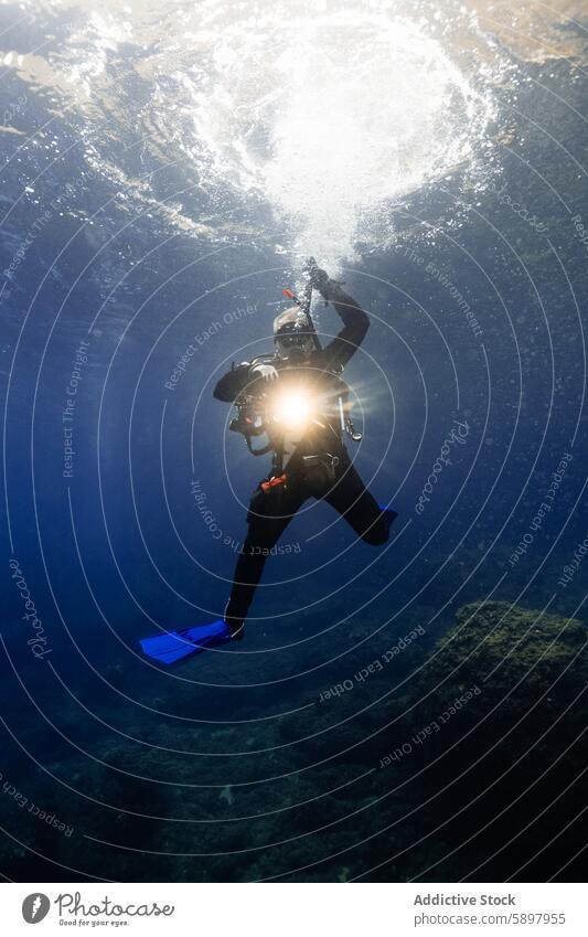 Male diver shines light underwater, showcasing deep-sea exploration male ocean adventure diving deep sea aquatic scuba gear camera sunlight marine blue depth