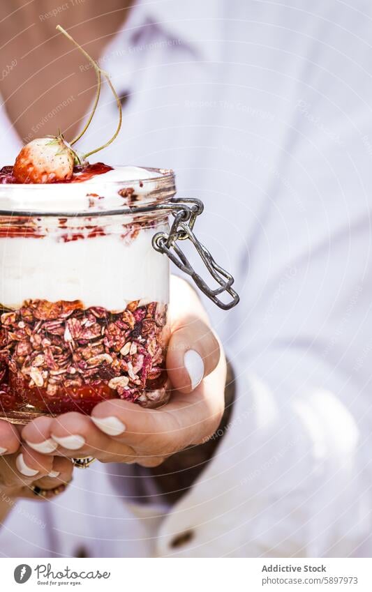 Close-up of a hand holding a jar of yogurt parfait with granola woman strawberry breakfast healthy summer fruit layer nutritious snack glass muesli oatmeal red