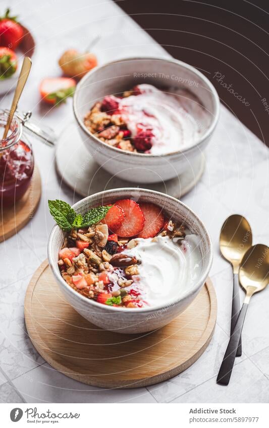 From above of a fresh yogurt bowl with fruits and granola breakfast summer strawberry raspberry jam topping healthy morning snack dairy nut almond wooden spoon