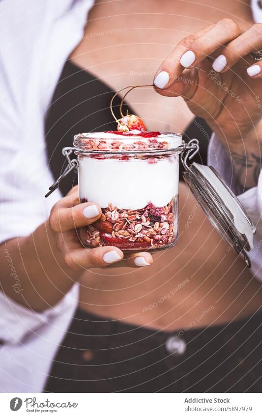 Woman holding a jar of yogurt parfait with fruits and granola summer breakfast healthy strawberry cherry woman hand unrecognizable anonymous faceless nutrition