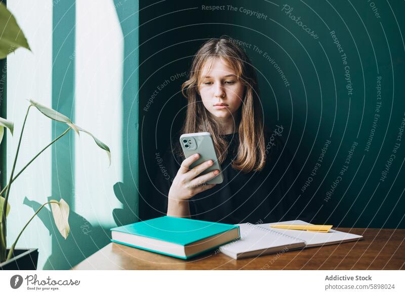 Young female student using smartphone while studying school backlit natural light peaceful books technology gadget mobile phone education youth teenager reading