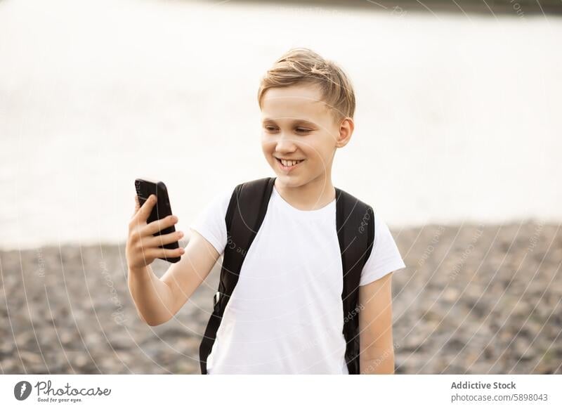 Teenager boy taking selfie with smartphone in park near a pond teenager mobile phone outdoor happy smiling looking at screen lake video vlog smile blogger