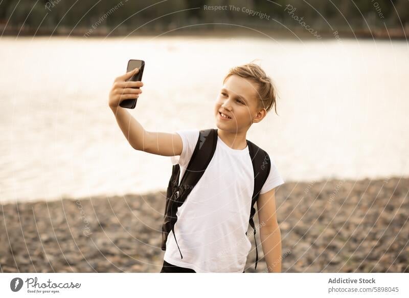Teenager boy taking a selfie with a smartphone in a park near a lake teenager mobile phone outdoor video vlog blogger traveller happy recording capturing