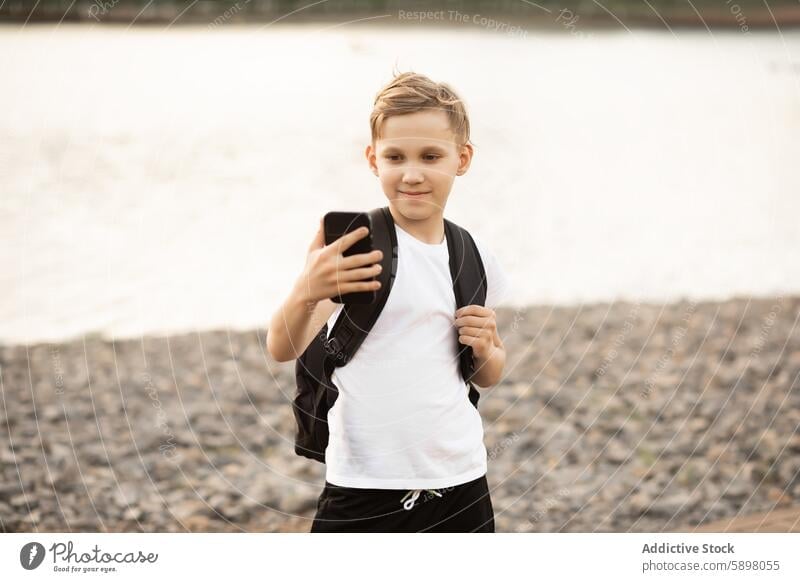 Teenage boy taking selfie in park near a lake with smartphone teenager mobile phone outdoor blogger traveller video vlog device gadget pond camera moment