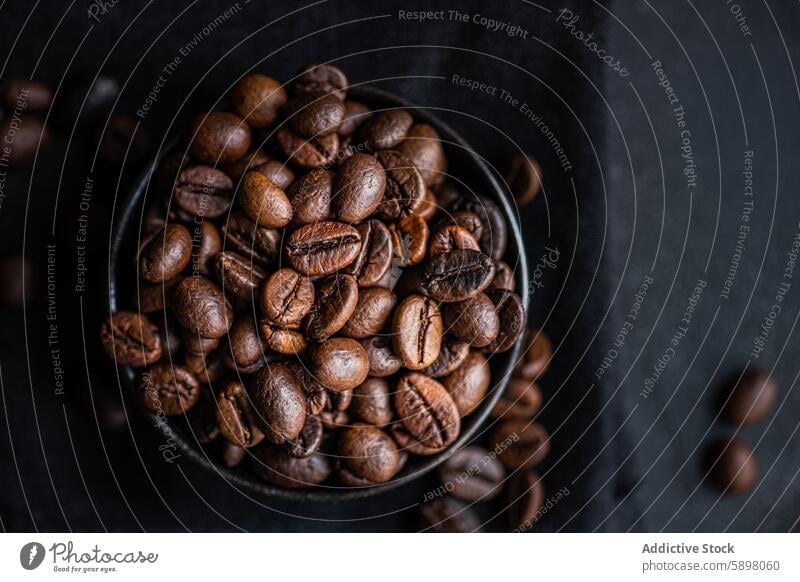 Aerial view of fresh whole coffee beans in a dark bowl texture brown glossy aromatic caffeine roast dark roast top close-up gourmet ingredient natural
