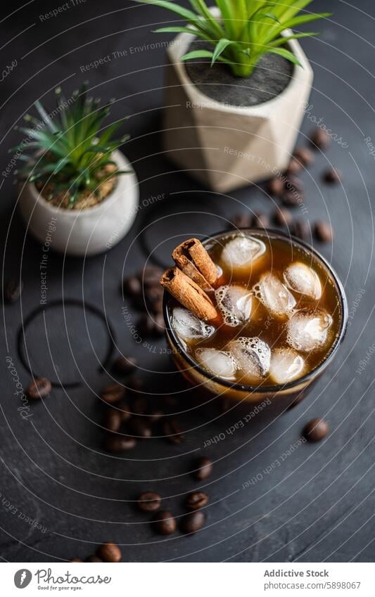 Top view of iced coffee with cinnamon and coffee beans beverage cold drink top view glass cube refreshment dark surface plant pot cozy aromatic brown black