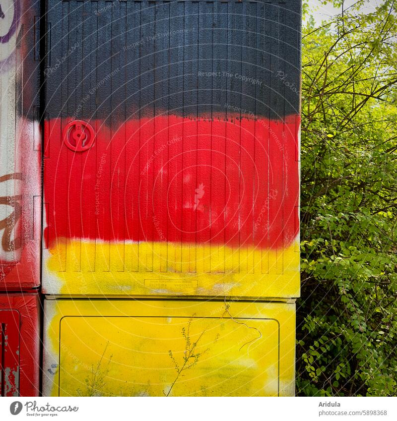 Black, red, yellow spray-painted electricity box with hedge Germany black-red-gold Colour Graffiti German Flag Ensign German flag Politics and state Patriotism