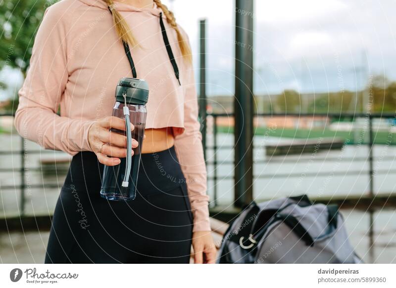 Young sportswoman with water bottle and gym bag unrecognizable athlete midsection hydration copy space crop top holding rainy training morning fitness active