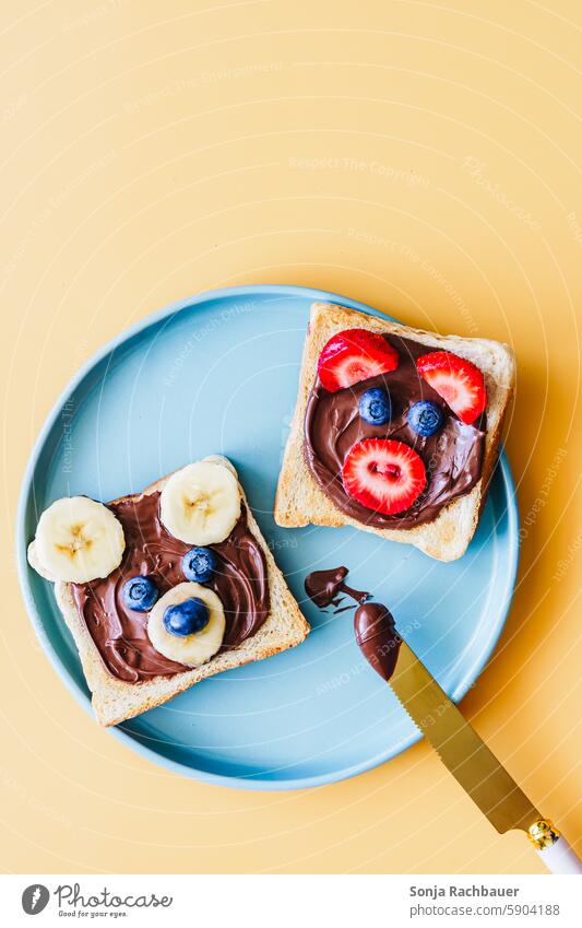 Two slices of toast with chocolate cream and funny animal faces made of fruit. Top view. Breakfast Child Toast Funny Animal face Infancy Plate plan