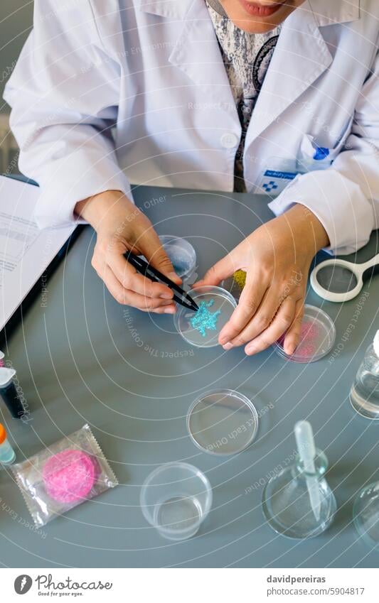 Unrecognizable female scientist analyzing a blue glitter sample over petri dish on laboratory unrecognizable scientific examining micro plastic analysis