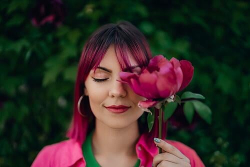 Portrait of real serene woman with vivid dyed pink fuchsia hairstyle. Peony flower, green nature backdrop. Trendy colorful hair, stylish haircut beautiful