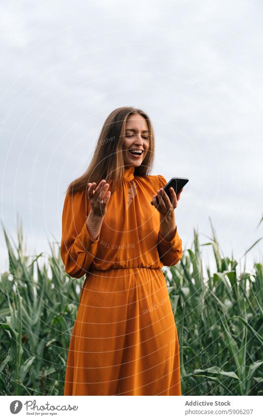 Brunette woman using smartphone in a cornfield brunette orange gown happy outdoor casual joy engagement mobile phone communication technology gadget smile