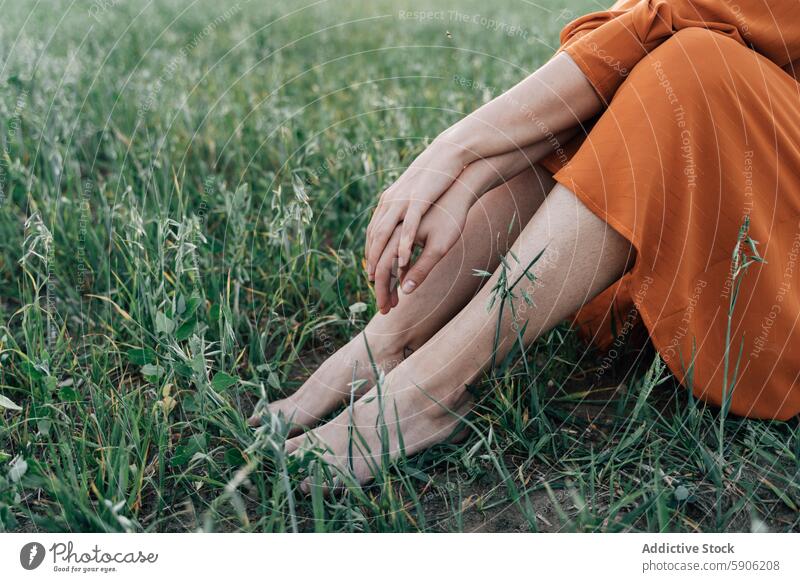 Cropped view of woman sitting alone in grassy field nature orange dress bare legs outdoor tranquility peace summer serene calm reflect connection earth