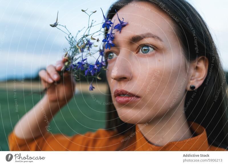 Brunette woman holding flowers in a field, looking away brunette nature contemplative wildflowers gaze connection outdoors portrait thoughtful natural female