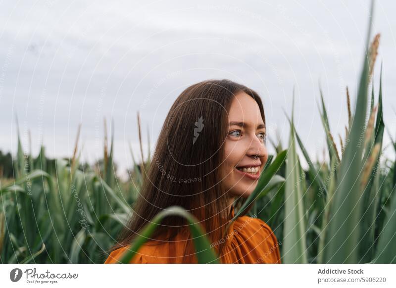 Brunette woman enjoying a serene moment in a green field brunette nature outside plants content smile looking away female peaceful orange blouse outdoors