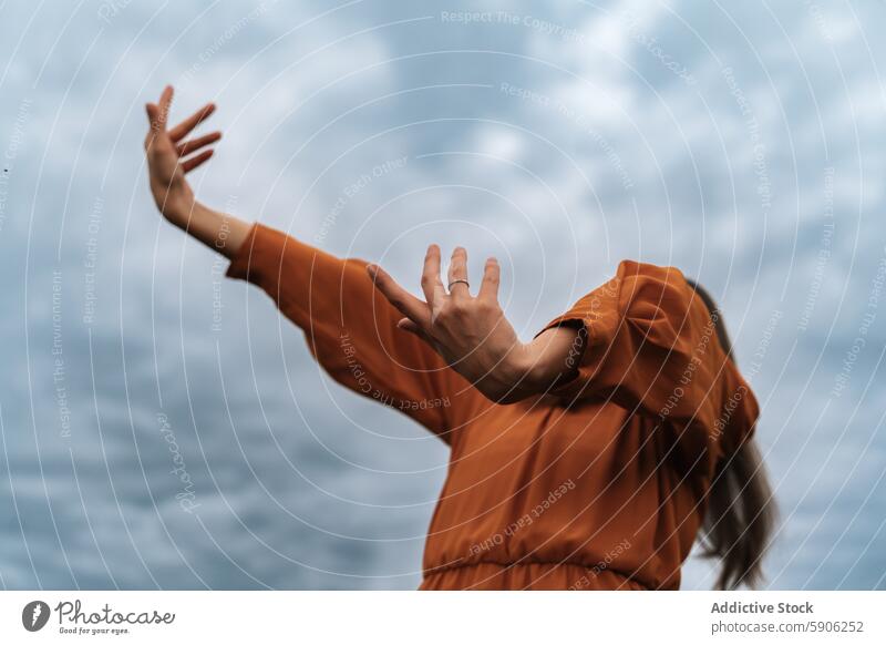 Woman in orange dress reaches out against cloudy sky woman brunette reaching hand field standing outdoor nature expression motion gesture fabric style