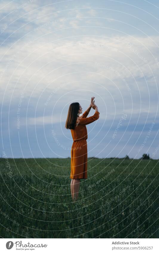 Woman in orange dress enjoying nature in a green field woman sky clouds outdoors gesture brunette summer grass fashion serene peaceful landscape casual leisure