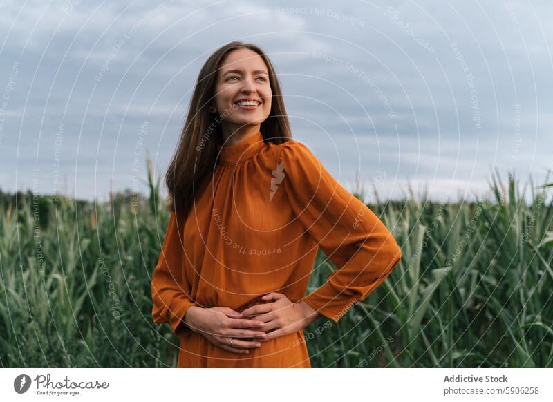 Brunette woman smiling in a field, looking away from camera grass brunette dress orange joy happiness outdoor nature rural peaceful serene summer female adult