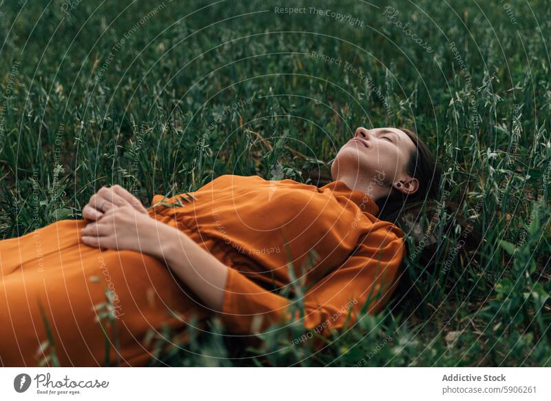 Woman in orange dress relaxing in green field woman brunette nature eyes closed tranquility grass outdoor summer serene peaceful meadow lying down leisure young