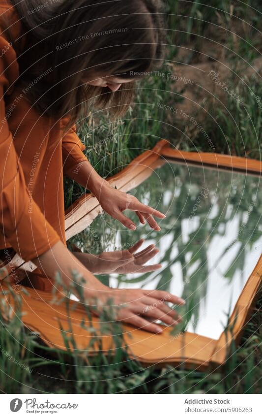 Brunette woman interacting with mirror in grassy field brunette reflection contemplation exploration outdoor nature serene tranquility summer dress orange cloth