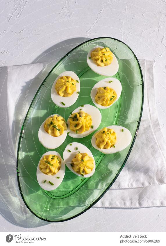 Delicious deviled eggs on a green glass platter, top view sunlight shadow white background chive garnish creamy yellow filling food appetizer snack gourmet