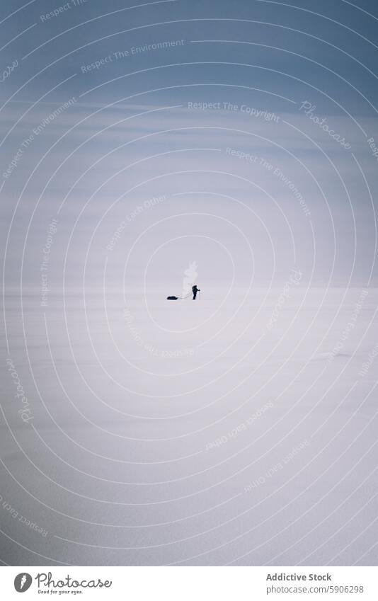 Solitary figure pulling sled in vast snowy landscape solitude minimalism sky cloudy cold winter endurance solitary white vastness unrecognizable anonymous