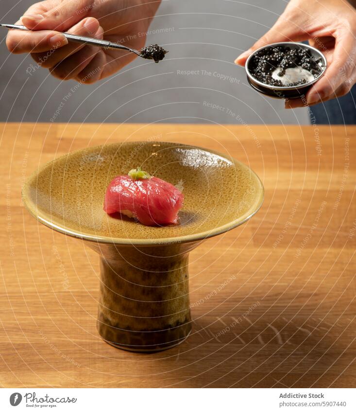 Adding the finishing touches to sushi with caviar garnish hand ceramic plate texture close-up seafood cuisine japanese delicacy preparation cooking chef detail