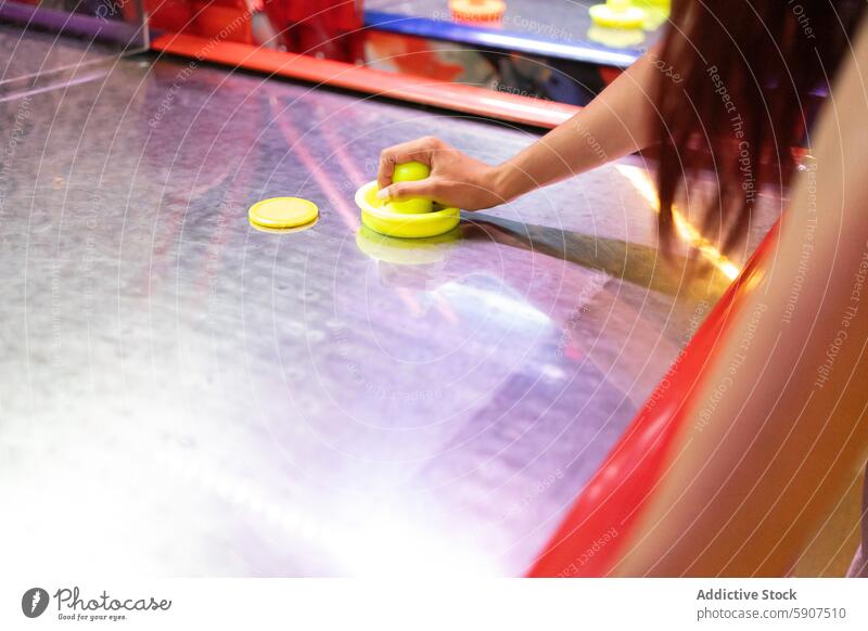 Anonymous woman playing air hockey at an indoor arcade game activity leisure entertainment focus sport table puck competitive excitement hand motion movement