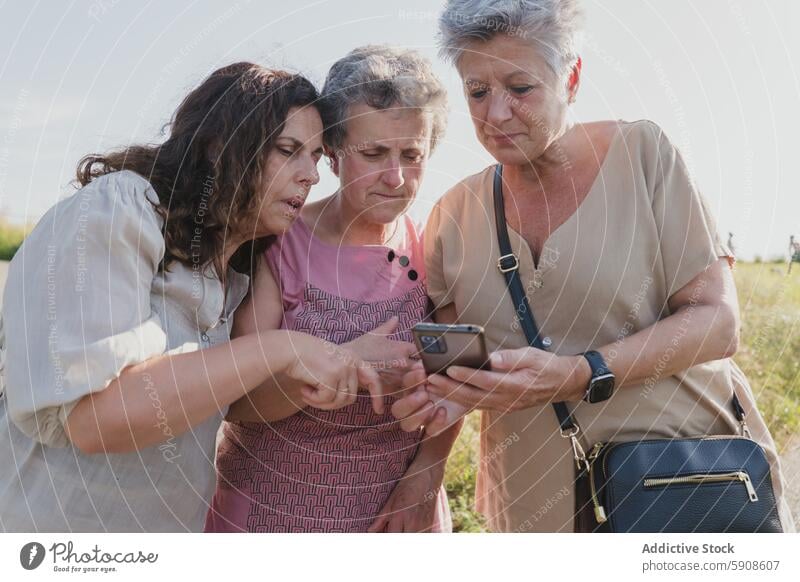 Three senior women sharing a moment with a smartphone elderly technology mobile phone gadget device outdoor friendship communication curious engaged connection