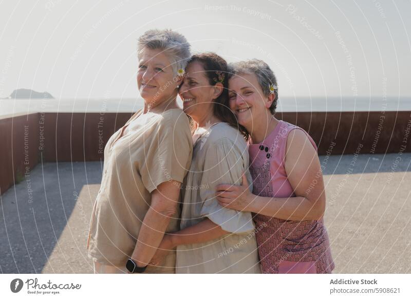 Elderly women embracing by the seaside, smiling together elderly friendship embrace looking at camera outdoors daylight sunny leisure love happiness bond mature