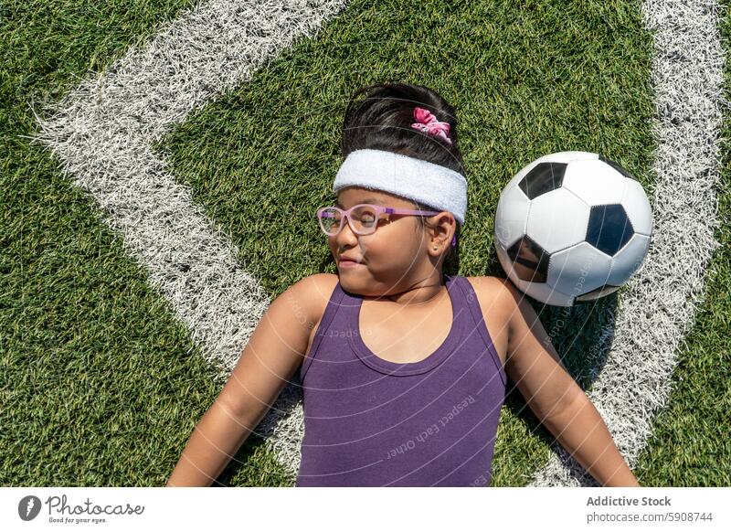 Young girl relaxing next to a soccer ball on field sport grass play joyful fitness leisure activity recreation outdoor summer fun happy child youth sporty