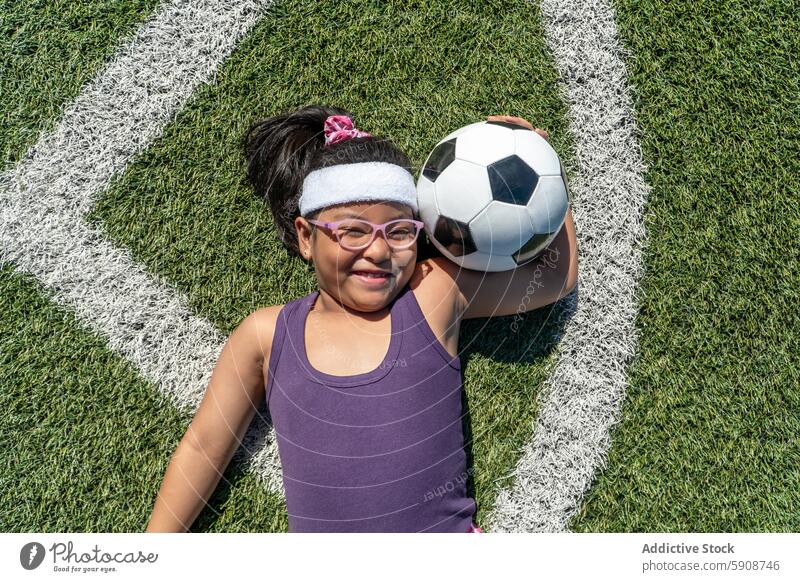 Smiling young girl holding a soccer ball on the field child sport grass outdoor play energy happy joy game smile glasses diversity inclusion youth health