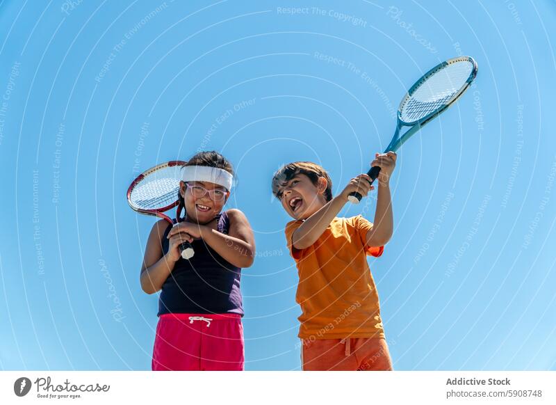 Joyful multiethnic children enjoying a game of tennis outdoors friendship sport racket play laugh happy excitement summer boy girl sky blue sunny day health