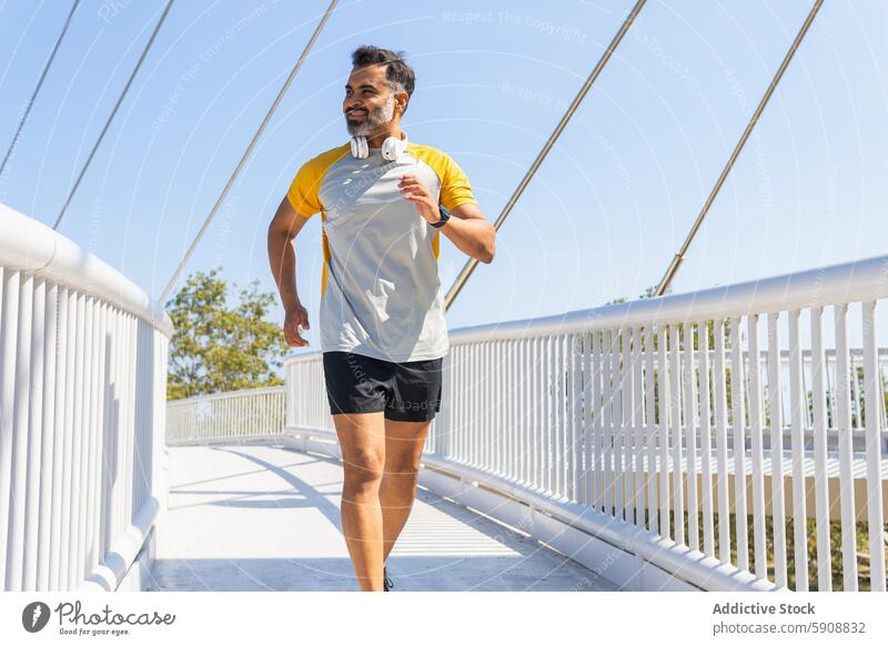 Indian man jogging on bridge with headphones in summer indian sportswear athlete running outdoor fitness exercise active lifestyle health wellness road railing