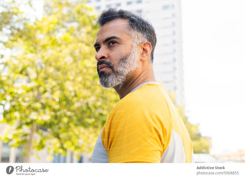 Indian man in sportswear looking away in summer setting indian urban park thoughtful standing outdoor city tree daytime fitness exercise healthy lifestyle male