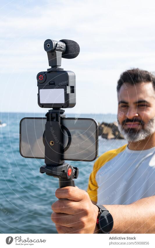 Man recording a video at seaside using modern gadgets indian man summer sport smartphone device camera stabilizer ocean technology male recorder outdoor water