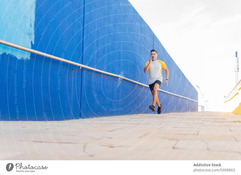 Indian man jogging in a summer setting against a blue wall indian jogger running sportswear outdoor sunny activity fitness exercise athlete health wellness