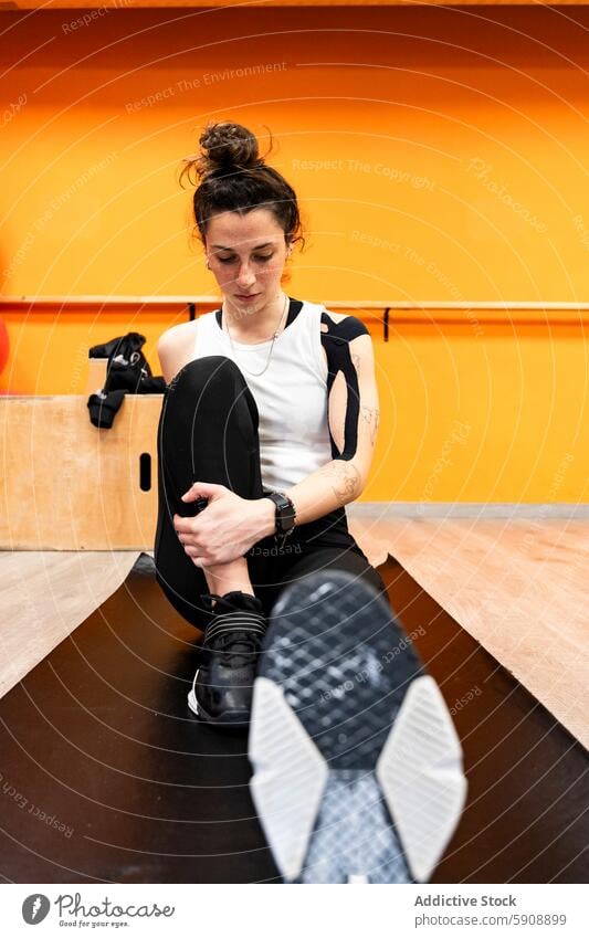 Young Woman Stretching Before Powerlifting Workout woman gym sportswear workout shoe sitting mat orange wall young athlete fitness powerlifting training