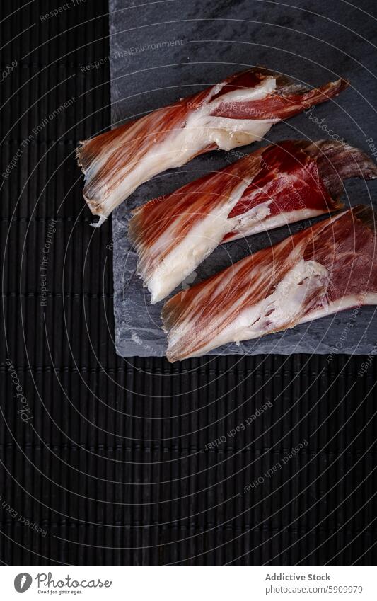 Slices of serrano ham on dark textured background slice spanish food slate board close-up marbled color contrast gourmet cuisine delicacy traditional culinary