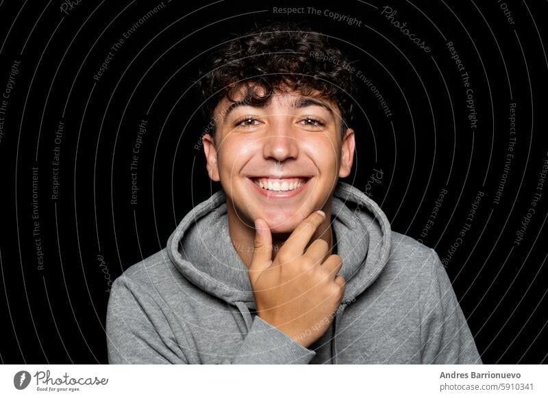 Portrait of young man about 25 years old with curly hair, holds hand on chin and smiles at camera. Isolated on black studio background dark 25s positive aged